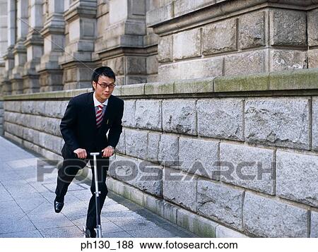 Asian Man riding a foot propelled scooter View Large Photo Image Stock Photo - Asian Man riding a foot propelled scooter. Fotosearch