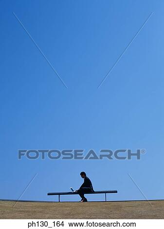 Picture - Asian Man sitting and working on his laptop. Fotosearch