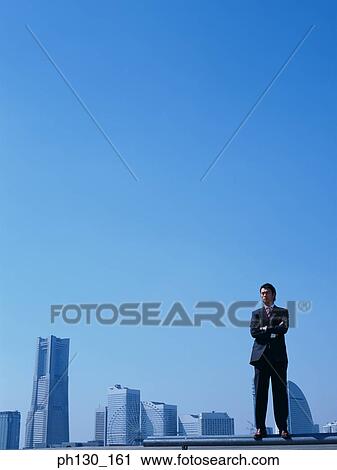 Stock Image - Asian Man standing in front of skyscrapers. Fotosearch