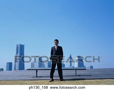 Stock Photo - Asian Man standing in front of skyscrapers. Fotosearch