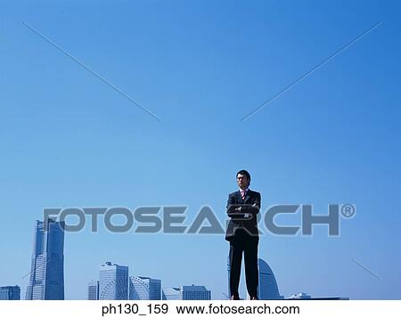 Stock Photo - Asian Man standing in front of skyscrapers. Fotosearch