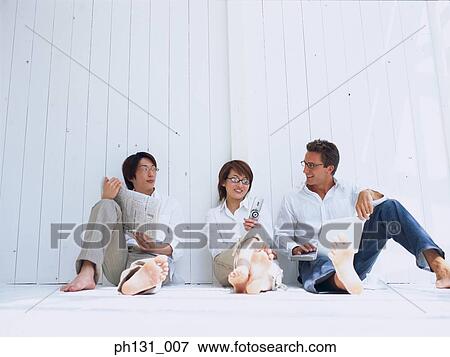 Stock Photo - A woman and two men sitting on the floor and talking. Fotosearch