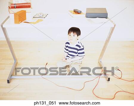 Stock Image - Asian child sitting under a desk. Fotosearch