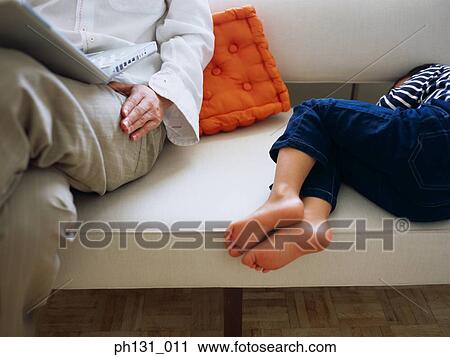 Stock Image - Father sitting on the couch with his sleeping son. Fotosearch