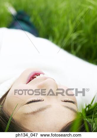 Young woman lying down on grass View Large Photo Image Stock Photo - Young woman lying down on grass. Fotosearch