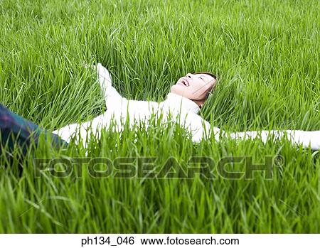 Young woman lying down on grass View Large Photo Image Stock Photograph - Young woman lying down on grass. Fotosearch