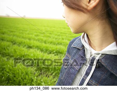 Stock Photograph - Young woman standing in a field looking back. Fotosearch