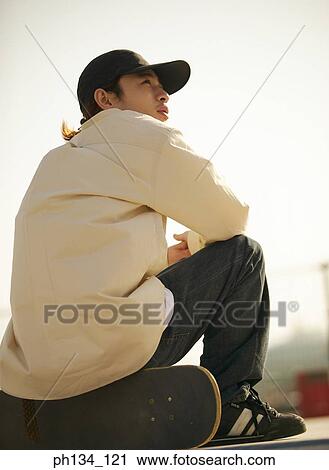 Stock Image - Young man sitting on a skateboard. Fotosearch