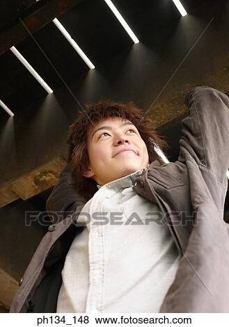 Young man standing with arms raised View Large Photo Image Stock Photo - Young man standing with arms raised. Fotosearch