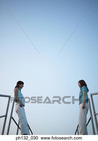 Two young women standing facing each other View Large Photo Image Stock Image - Two young women standing facing each other. Fotosearch