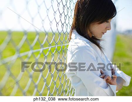 Stock Photo - Young woman leaning on a chain_link fence. Fotosearch