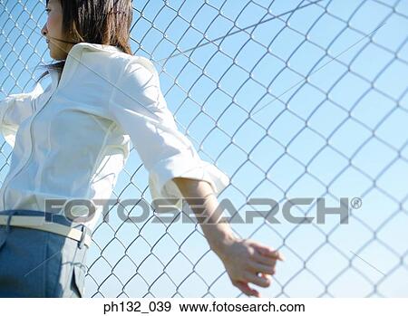 Stock Photo - Young woman leaning on a chain_link fence. Fotosearch