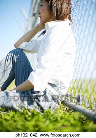 Stock Image - Young woman on the ground leaning on a chainlink fence. Fotosearch