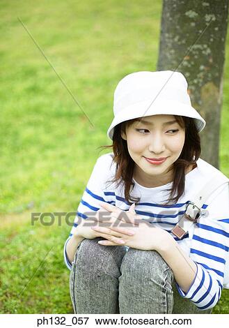 Stock Photo - Young woman sitting leaning against a tree. Fotosearch