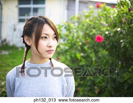 Stock Image - Young woman standing in a garden. Fotosearch