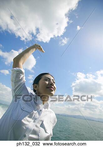 Stock Image - Young woman waving by the shore. Fotosearch