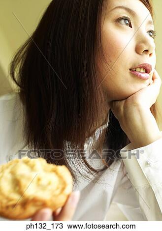 Stock Image - Young woman holding out a cookie. Fotosearch