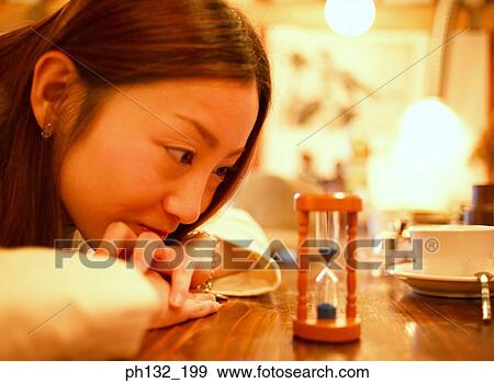 Young woman looking at an hourglass View Large Photo Image Stock Photo - Young woman looking at an hourglass. Fotosearch