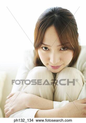 Picture - Young woman sitting hugging her knees. Fotosearch