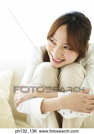 Stock Photograph - Young woman sitting hugging her knees. Fotosearch