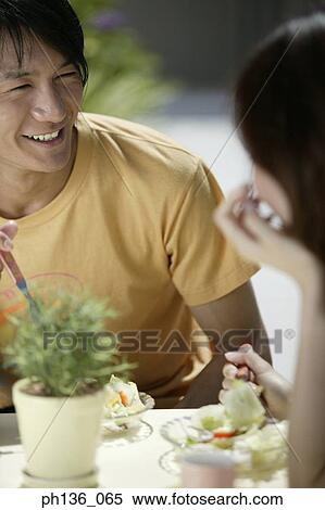 Stock Photography - Young couple seated at a dining table laughing. Fotosearch