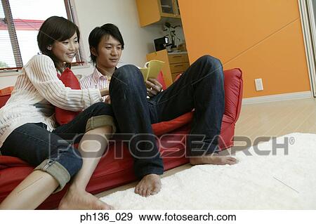 Stock Photo - Young couple sitting on a couch reading a book. Fotosearch