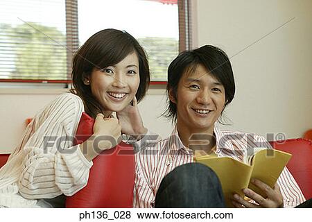 Young couple sitting together on a couch looking at camera View Large Photo Image Stock Photo - Young couple sitting together on a couch looking at camera. Fotosearch