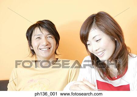 Stock Image - Young couple sitting together smiling. Fotosearch