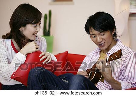 Stock Image - Young man playing a guitar and a woman sitting beside. Fotosearch