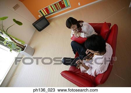 Stock Image - Young man playing a guitar and a woman sitting beside. Fotosearch