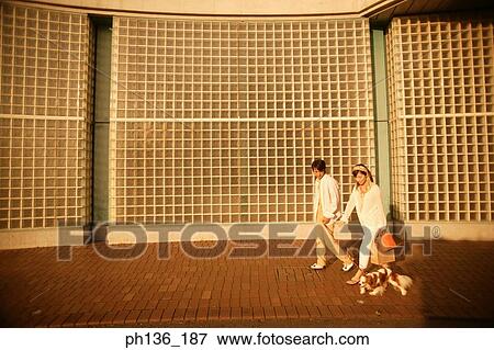 Stock Photo - Young couple walking with a pet dog. Fotosearch