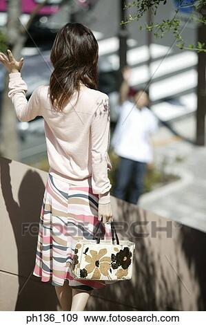 Young woman standing holding a hand bag View Large Photo Image Stock Photo - Young woman standing holding a hand bag. Fotosearch
