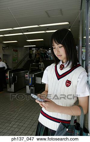 Stock Photo - Teenage girl Leaning against wall operating mobile phone. Fotosearch