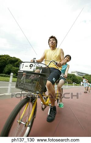 Stock Image - Teenagers riding a tandem bicycle. Fotosearch