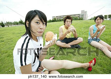 Teenagers sitting on a lawn eating hamburgers View Large Photo Image Stock Image - Teenagers sitting on a lawn eating hamburgers. Fotosearch