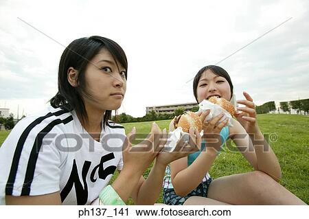 Stock Image - Teenagers sitting on a lawn eating hamburgers. Fotosearch