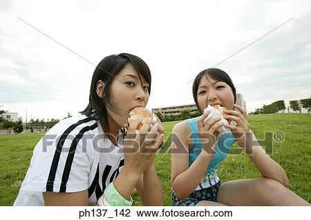 Stock Image - Teenagers sitting on a lawn eating hamburgers. Fotosearch