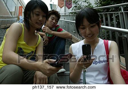 Stock Photo - Teenagers sitting together operating their mobile phones. Fotosearch