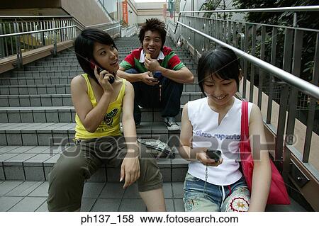 Teenagers sitting together operating their mobile phones View Large Photo Image Stock Photo - Teenagers sitting together operating their mobile phones. Fotosearch