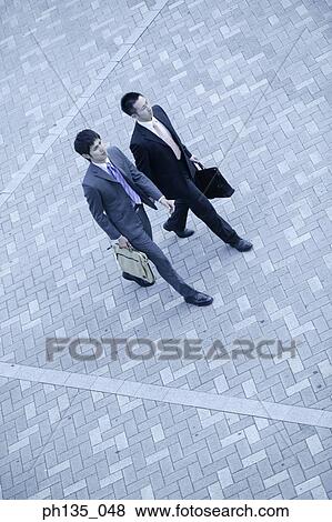 Stock Photo - High angle view of two young businessmen walking outdoors. Fotosearch