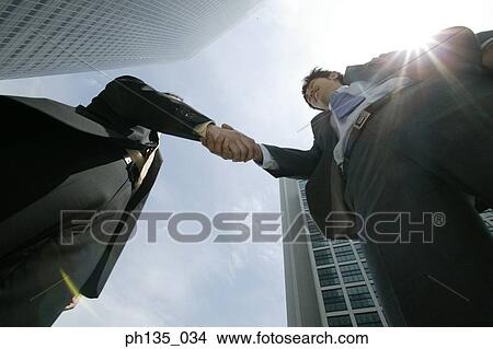 Picture - Low angle view of two young businessmen shaking hands. Fotosearch