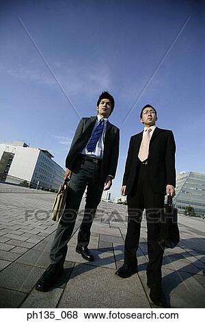 Stock Photo - Low angle view of two young businessmen standing outdoors. Fotosearch