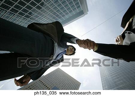 Low angle view of two young businessmen shaking hands View Large Photo Image Stock Photography - Low angle view of two young businessmen shaking hands. Fotosearch