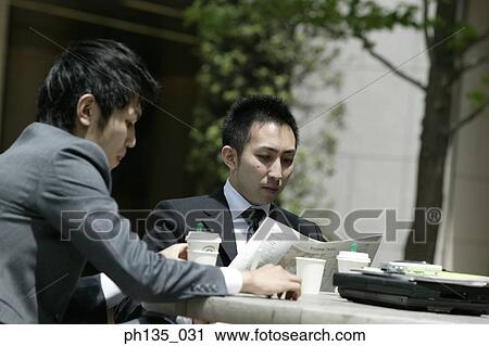 Stock Image - Two young businessmen having coffee at an outdoor cafe. Fotosearch