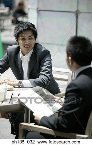 Two young businessmen having coffee at an outdoor cafe View Large Photo Image Stock Image - Two young businessmen having coffee at an outdoor cafe. Fotosearch