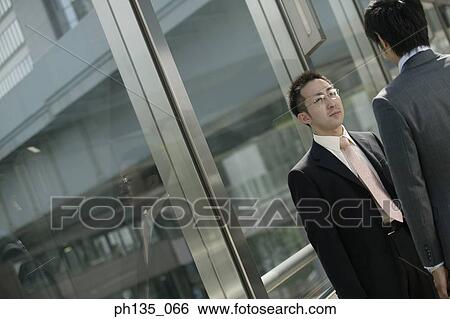 Stock Photograph - Two young businessmen talking in the passageway of an office. Fotosearch