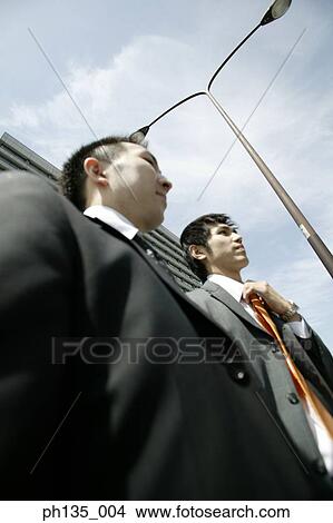 Picture - Two young businessmen waiting on a sidewalk. Fotosearch