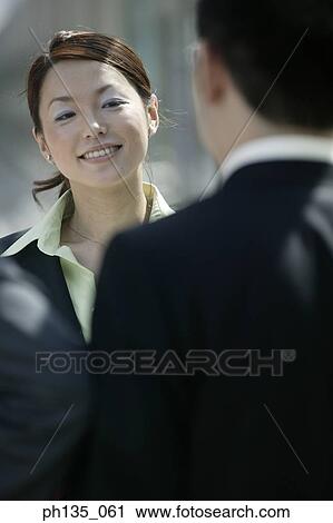 Young businesswoman talking to young businessmen standing across her View Large Photo Image Stock Image - Young businesswoman talking to young businessmen standing across her. Fotosearch