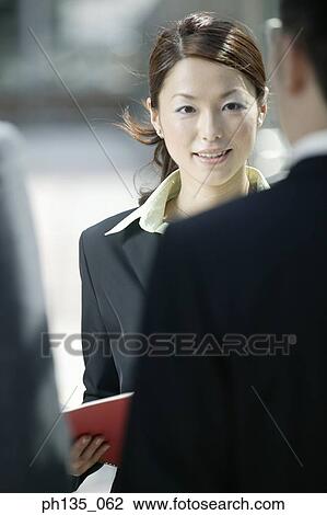 Young businesswoman talking to young businessmen standing across her View Large Photo Image Stock Image - Young businesswoman talking to young businessmen standing across her. Fotosearch