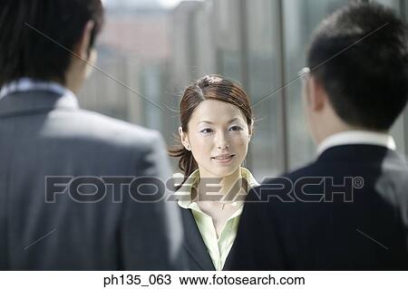 Young businesswoman talking to young businessmen standing across her View Large Photo Image Stock Image - Young businesswoman talking to young businessmen standing across her. Fotosearch